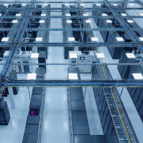 A data hall seen from above, rack rows between lit ceiling panels and cable runs